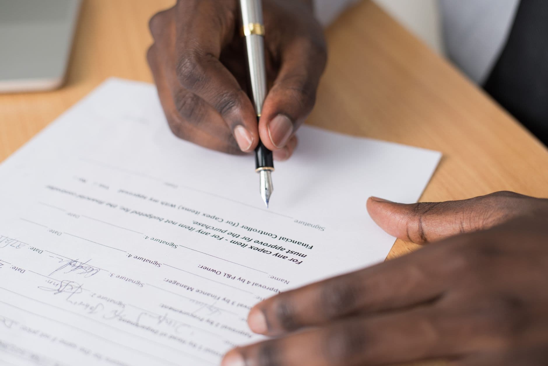 Nærbilde av hender som signerer et dokument med fyllepenn
